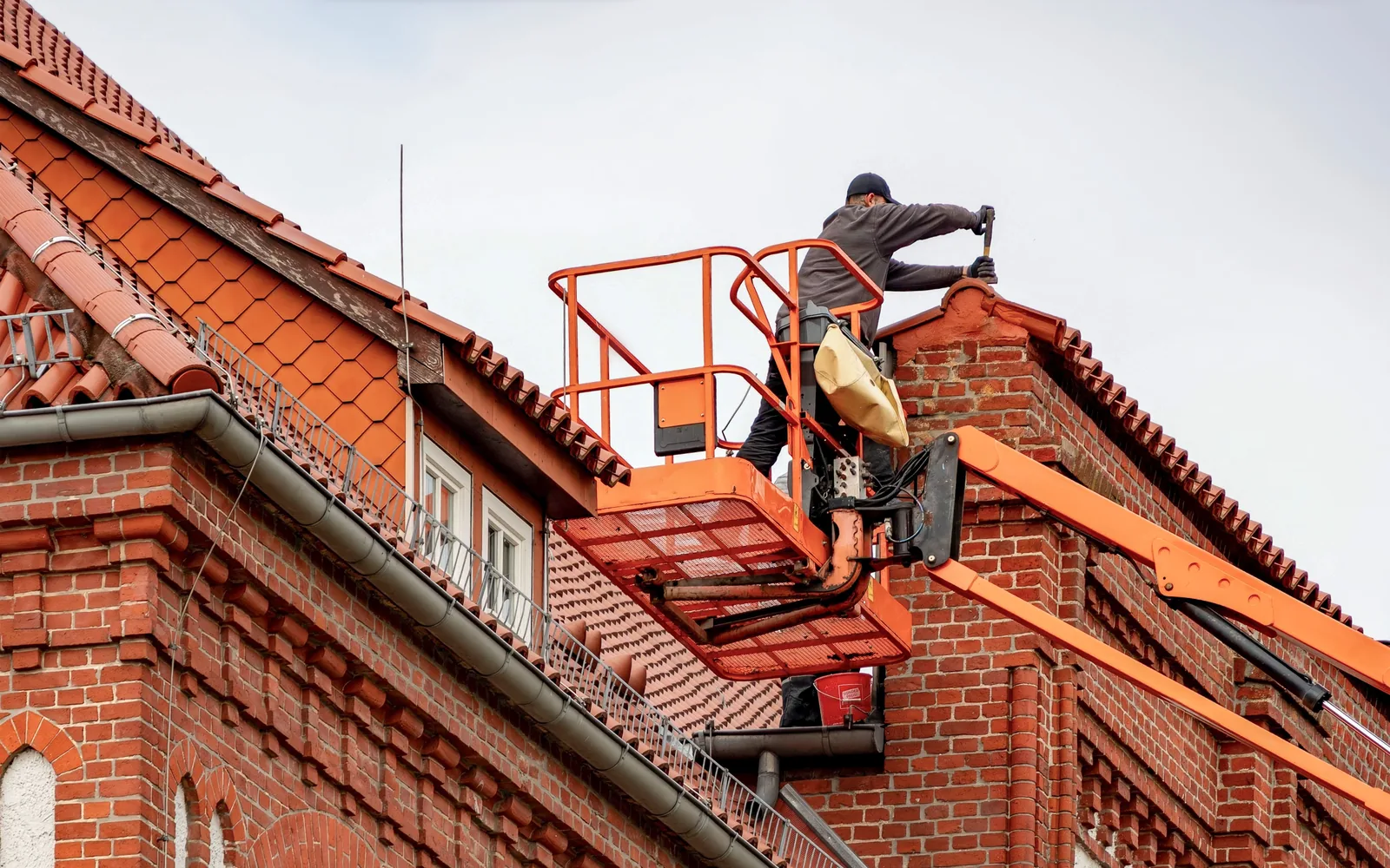 Roofing worker using a lift to perform maintenance on a tiled commercial building.