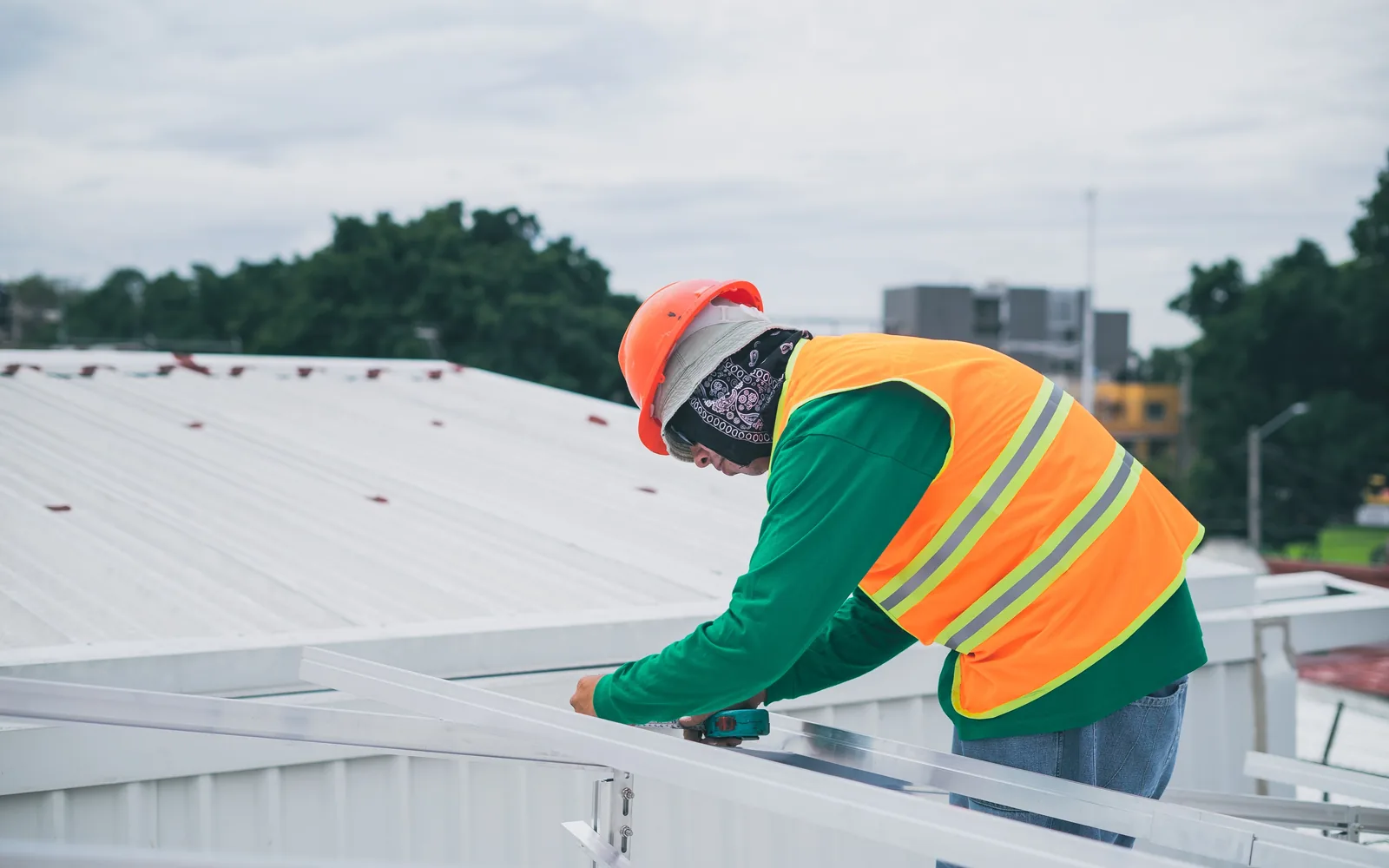 Commercial roofing worker wearing safety gear while fastening metal roof components.