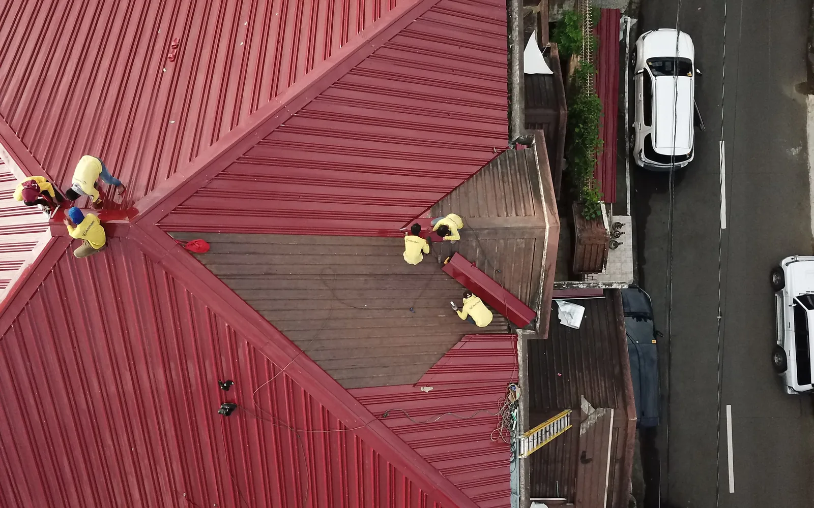 Roofing crew repairing and installing red metal roof panels from an overhead view.