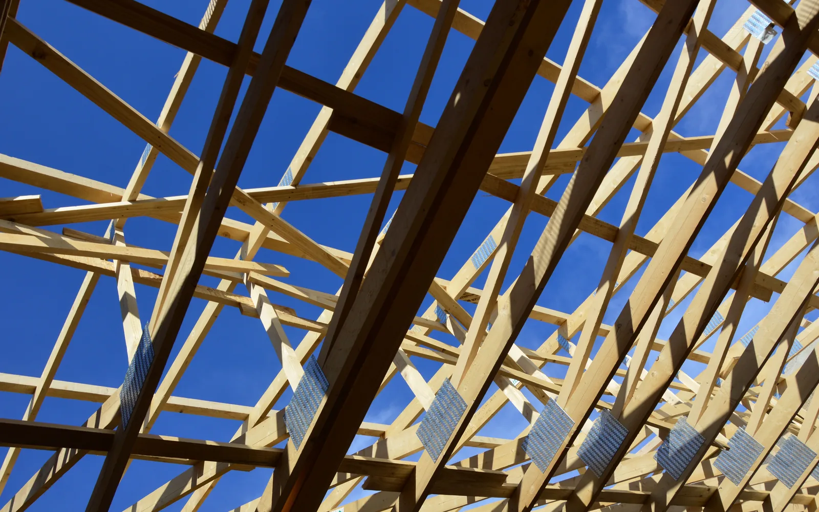 Wood roof trusses and structural framing under a bright blue sky.