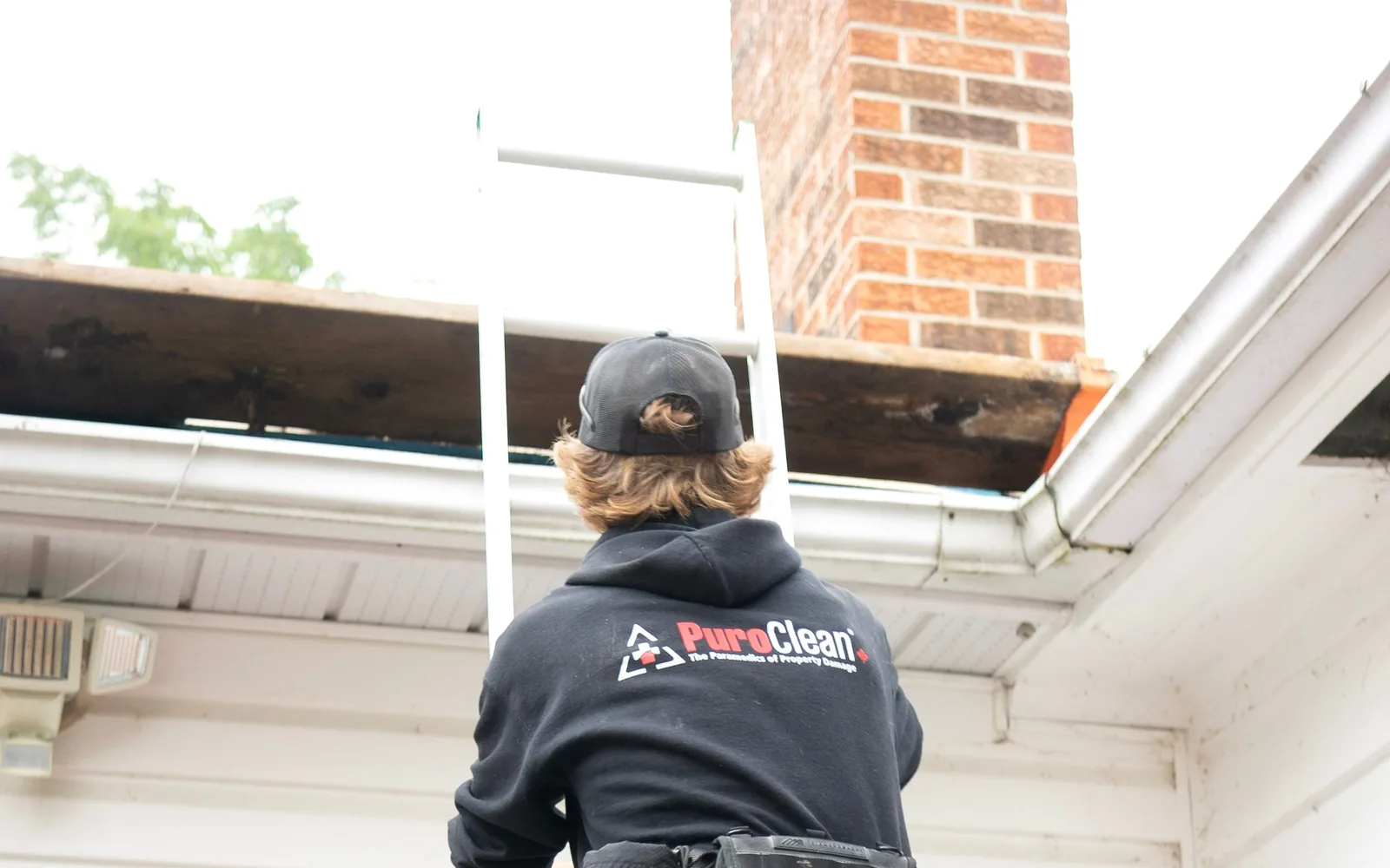 Roofing professional accessing a residential roof near a brick chimney.