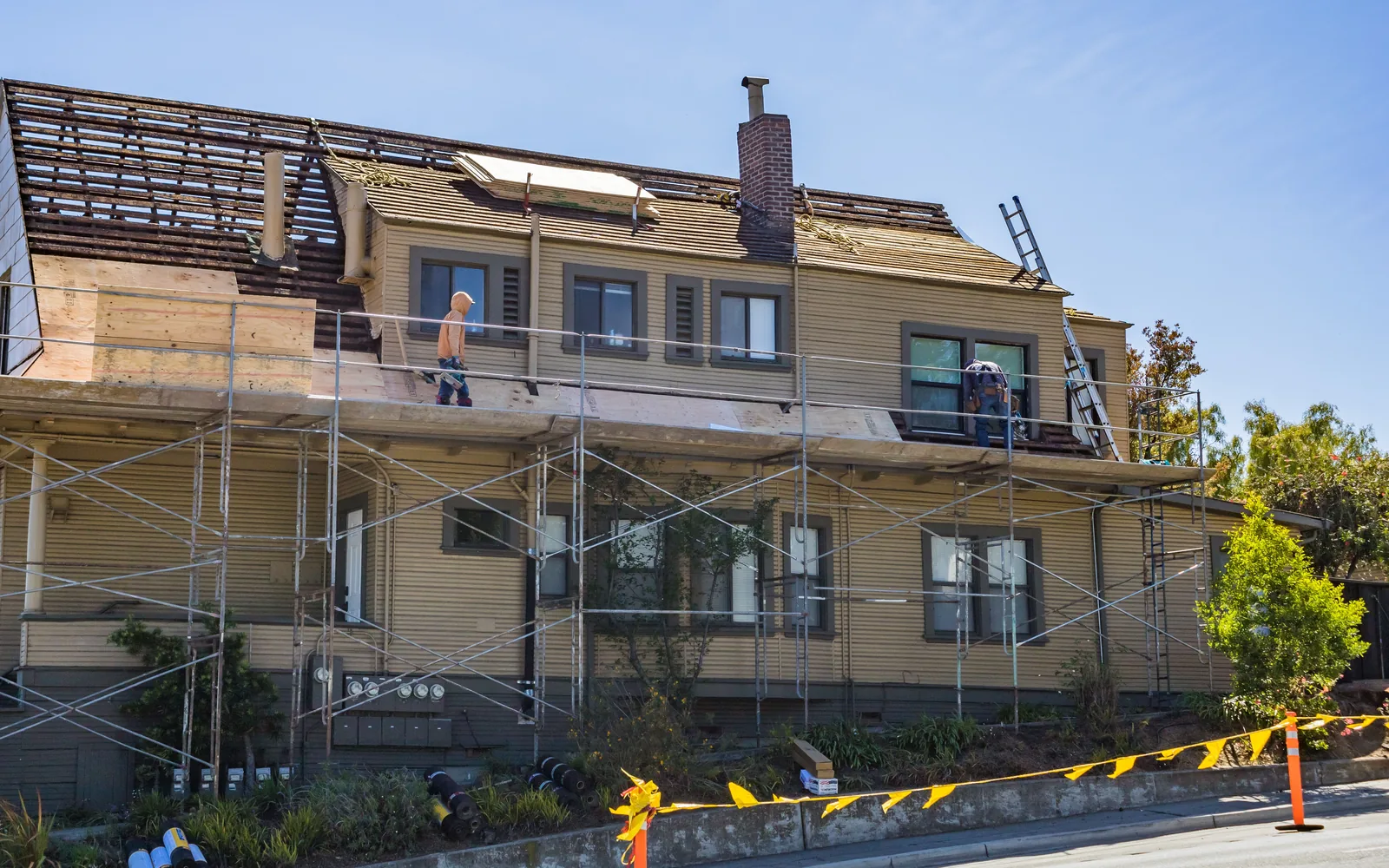 Large older home undergoing roof replacement with scaffolding and exposed roof decking.