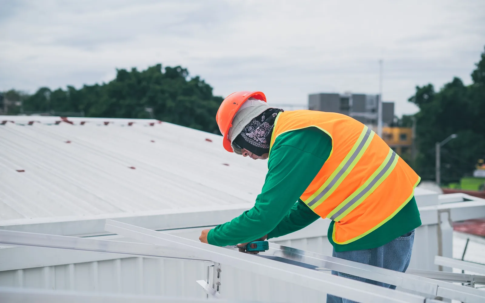 Roofing worker in high-visibility safety gear fastening roof components.