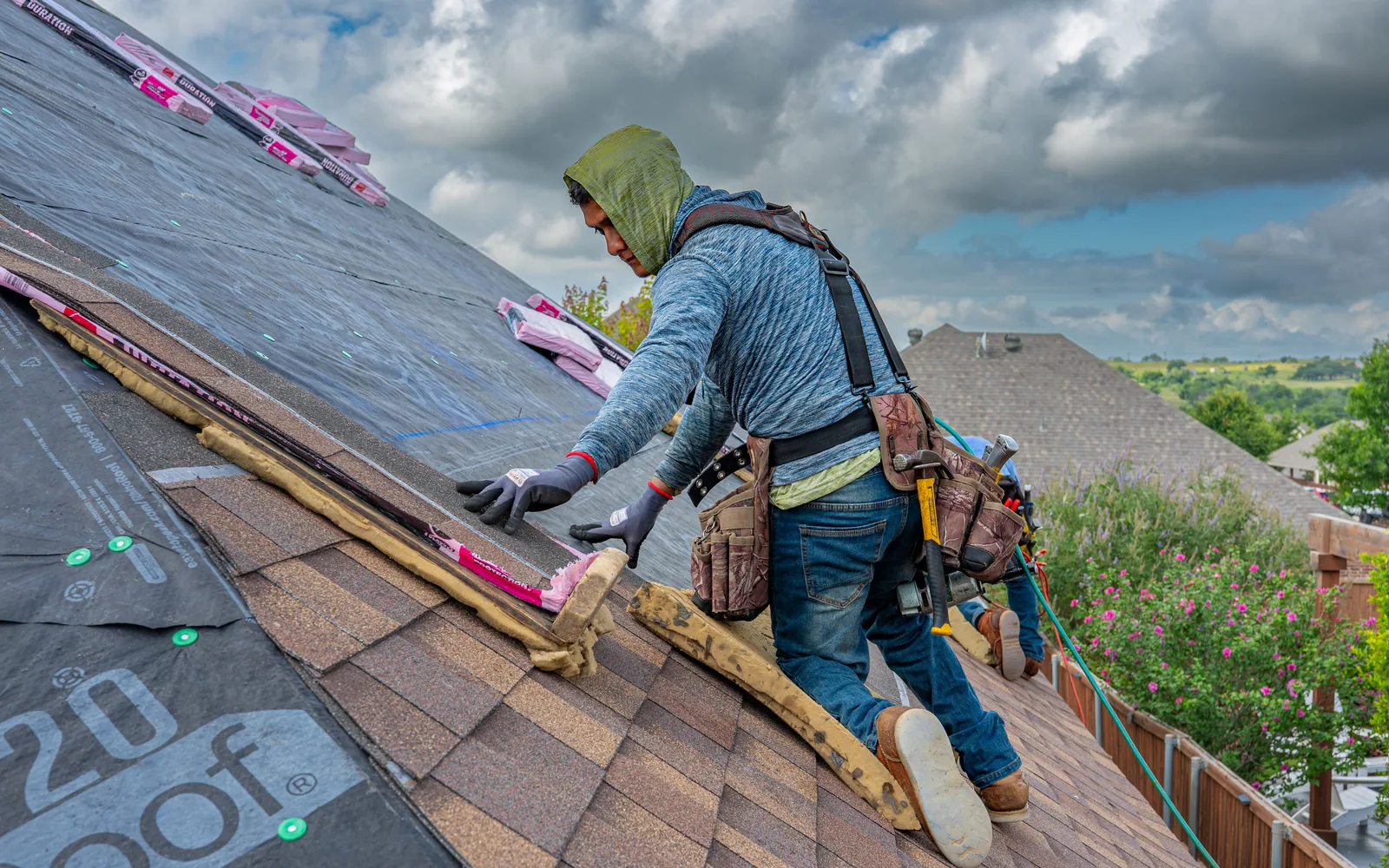 Roofer installing shingles over a prepared roof deck and synthetic underlayment.