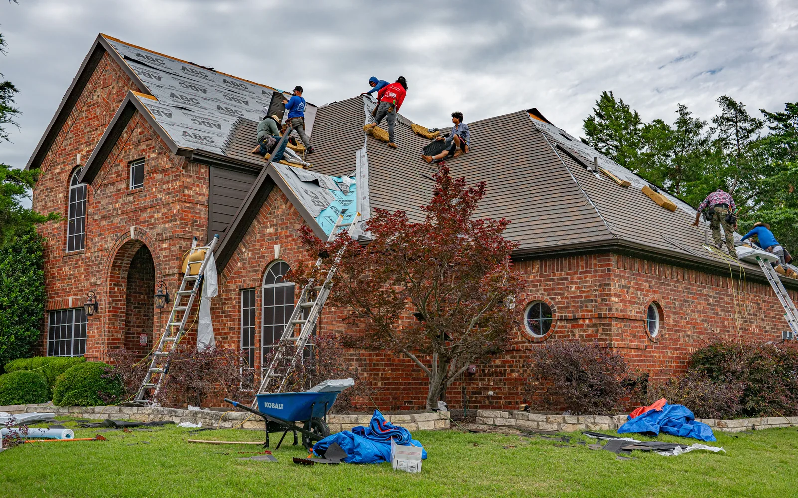 Roofing crew replacing asphalt shingles on a large residential home.