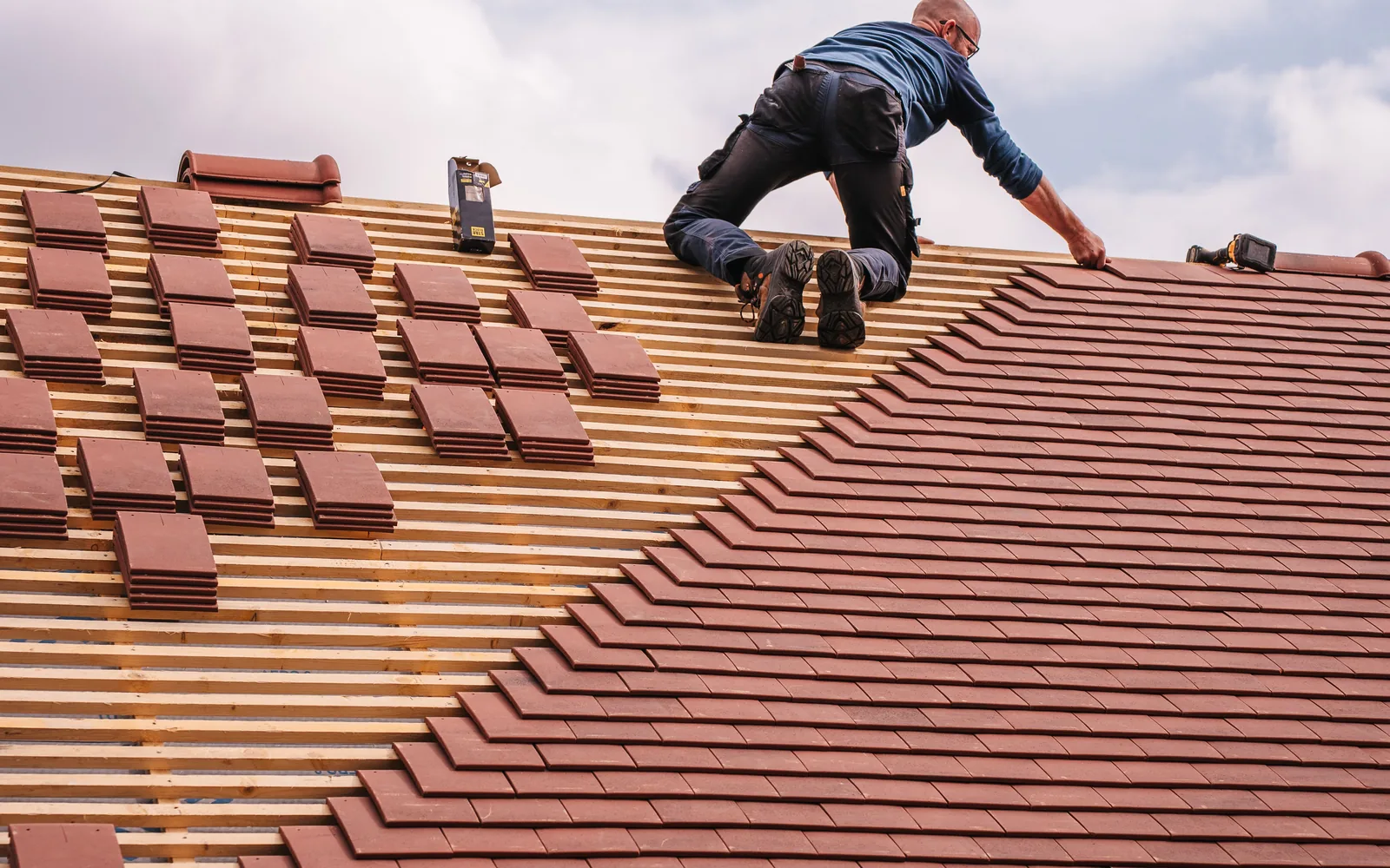 Roofing contractor installing red roof tiles on a steep residential roof.