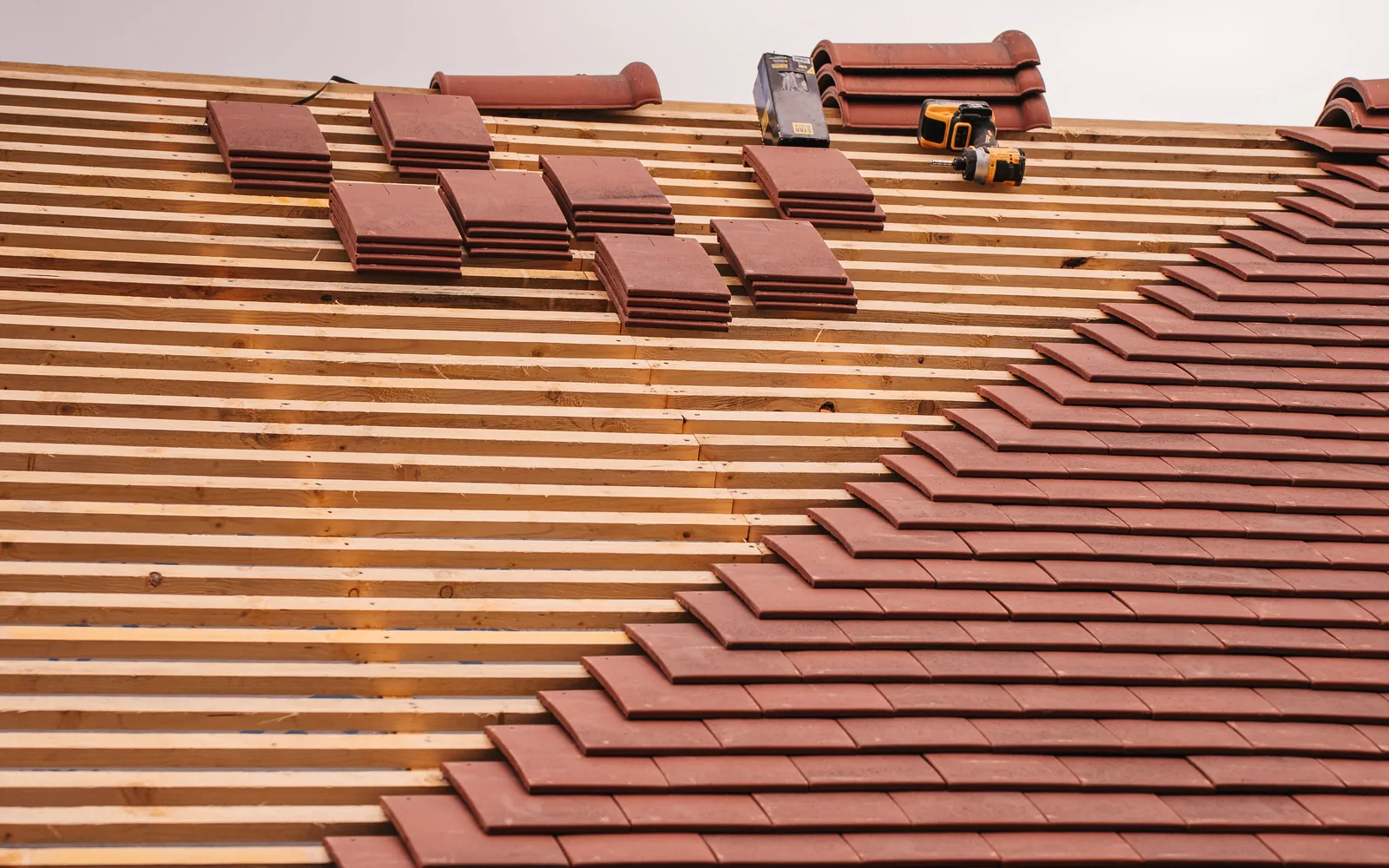 Partial installation of red concrete or clay roof tiles over roof battens.